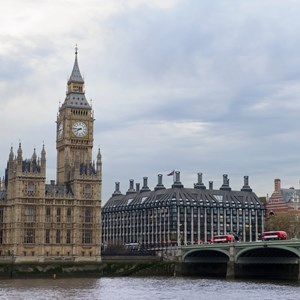 A photograph of the neo-gothic Palace of Westminster with Big Ben clock tower next to Westminster Bridge, with red buses crossing the bridge