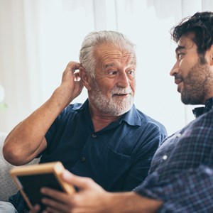 A man sits on a sofa speaking to his older father