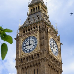 Elizabeth Tower with blue sky  behind and greenery in the foreground. A plane is flying overhead in the distance